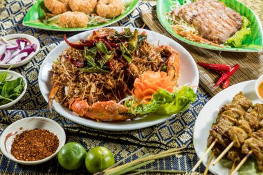 Kızarmış yengeç, domuz şişi, susamlı malzeme ve biberli ve limonlu otla servis edilen Tayland usulü tabaklar..