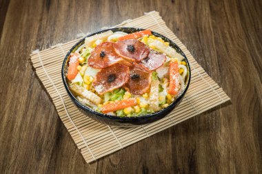 Biberli, erişteli, mısır, marul, havuç, peynir ve siyah garnitürlü renkli bir salata kasesi..