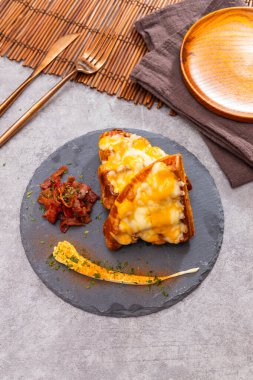 Eritilmiş peynirle kaplanmış kruvasan yarıları, domuz pastırması ve sosla servis edilmiş kırsal dekoru olan tahta tabakta..