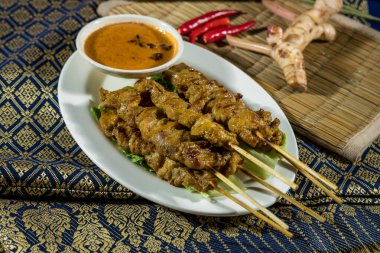 Tayland usulü satay şiş, marulda kremalı fıstık sosu, biber ve desenli kumaş üzerinde galangal servis edilir..