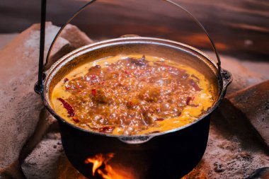 Bir tencere baharatlı sıcak çorba ocakta kaynıyor. Kırmızı biberler ve buhar yükseliyor. Çiğ et yemek için yakınlarda bekliyor..