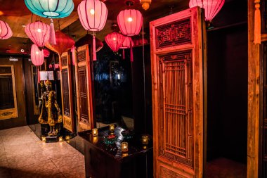 Fenerlerle, oyulmuş odunlarla, heykellerle, mumlarla ve ayna yansımalarıyla Asya temalı bir iç mekan..