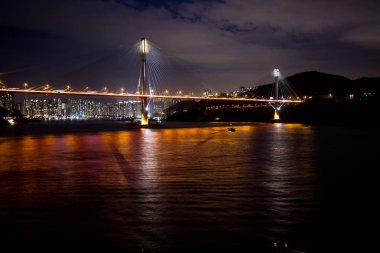 Bir kablo, geceleri su üzerindeki yansımalarla ve arka planda canlı bir şehir siluetiyle köprüde kaldı..