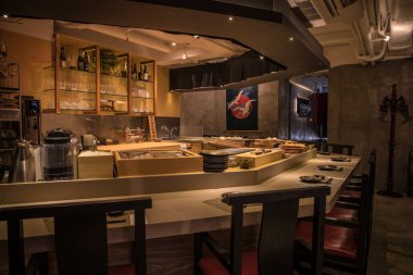 Japon tarzı bir restoranda kırmızı minderli sandalyeli, zarif yer ayarlı ve sıcak ışıklandırmalı U şeklinde bir suşi barı..