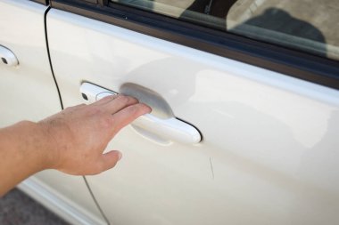 Beyaz bir arabanın kapı koluna doğru uzanan, lekeleri ve yansımaları gösteren, günlük araç etkileşimini kaydeden bir el..