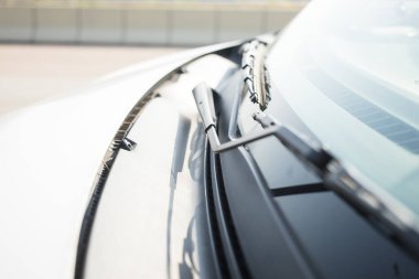 Arabanın ön camının yakın çekimi, silecek kolları altta, ışığı yansıtıyor ve arka planda bulanık bir yol bariyeri gösteriyor..