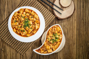 Baharatlı soslu iki porsiyon Mapo Tofu ve yeşil soğan garnitürü, yuvarlak ve yin-yang şeklinde tabaklar..