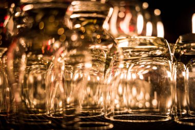 Sıcak ışık ve yansımalarla sıralanmış baş aşağı duran cam bardaklar dramatik ve sanatsal bir kompozisyon oluşturur..