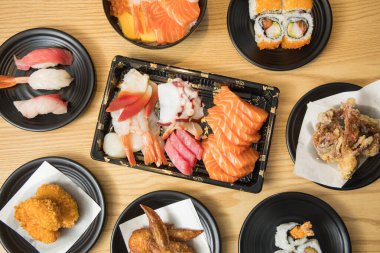 Japon yemeği, sashimi, nigiri, chirashi, sushi roll, karaage, kroket ve kızarmış kanat, siyah tabaklar ve kaseler üzerine dizilmiş..
