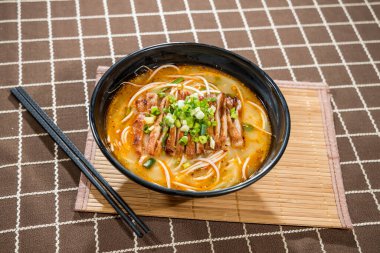 Bir kase portakal suyu, erişte, ızgara et dilimleri ve yeşil soğan garnitürlü Japon eriştesi bambu hasırıyla servis edilir..