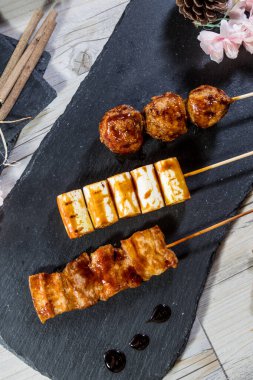 Üç Japon yakitori şiş tabağı: köfte, tofu veya balık keki ve ızgara et, jöleli ve sanatsal dekorasyonla servis edilmiş..