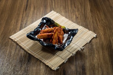 Kırmızı sosla kaplanmış bir kase baharatlı tavuk ayağı seramik bir kasede bambu hasırla servis edilir..