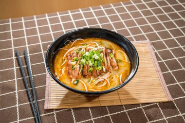 Bir kase portakal suyu, erişte, ızgara et dilimleri ve bambu hasırında yeşil soğan garnitürü..