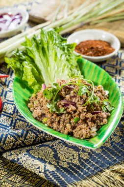 Tayland usulü domuz eti, kırmızı soğan, yeşil soğan, kişniş, limon suyu, yaprak şeklinde bir tabakta marul ve biber tozu ile servis edilir..