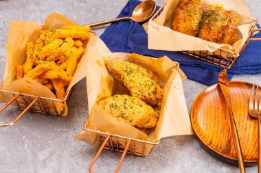 Kızarmış tavuk ve baharatlı patates kızartması bakır sepetlerde servis edilir, otlarla süslenir, altın kaplar ve koyu peçetelerle süslenir..