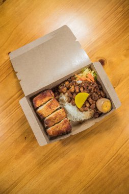 İçinde pilav, haşlanmış domuz eti, kızarmış et dilimleri, haşlanmış yumurta, turp turşusu ve doğranmış sebze olan bir paket..