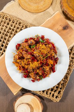 Etli baharatlı kızartma, kurutulmuş biber, yeşil soğan ve ezilmiş biber taneleri, beyaz bir tabakta servis edilir..