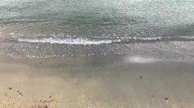 Sakin bir öğleden sonra deniz kenarında yumuşak kumlu kıyılara doğru hafif dalgalar süzülür.