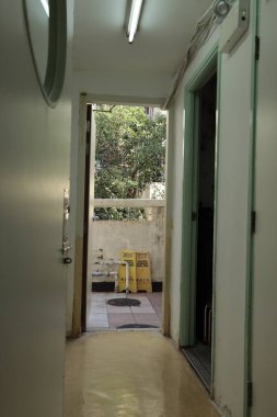 Yeşil çerçeveli kapıları olan parlak bir koridor, uyarı işaretleri ve beton parmaklıkların ardındaki yapraklı ağaçlarla dolu bir açık araziye açılıyor..