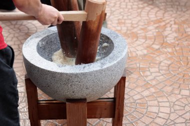 Geleneksel bir mochitsuki sahnesi. Kültürel takım çalışmalarını vurgulayan, taştan bir havan topunda buğulanmış pirinci dövmek için tahta tokmak kullanan iki kişi..