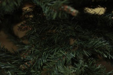 Doğal yaprakları taklit eden yeşil ve kahverengi plastik iğneli yapay çam dallarından loş bir yakın plan..