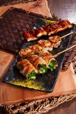 Sığır etine sarılı ızgara enoki mantarları, susam tohumları serpiştirilmiş, sos ve orkide garnitürü ile servis edilmiş..