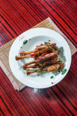 Kırmızı biber ve otlarla süslenmiş ızgara tavuk budu tabağı, çiçekli beyaz bir tabakta servis edilir..