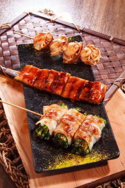 Üç şişe deniz tarağı, jöleli domuz eti ve ete sarılmış sebzeler benekli siyah bir tabakta servis ediliyor..