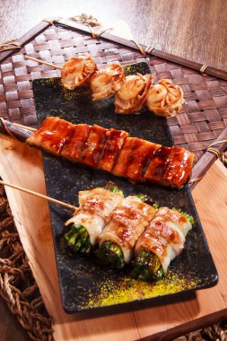 Üç şişe deniz tarağı, jöleli yılan balığı ve ete sarılmış sebzeler benekli siyah bir tabakta servis ediliyor..