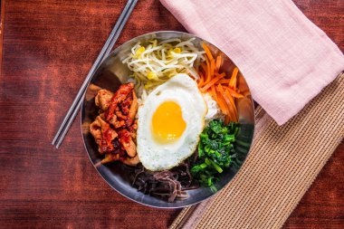 Bir kase bibimbap, pilav, yumurta, et, ıspanak, mantar, havuç, fasulye filizi ve kırmızı sos..
