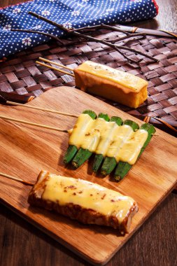 Üç Japon tarzı şiş, iki tane tavuk ya da tofu ve bir tane de erimiş peynir soslu bamya. Köy tahtasında servis ediliyor.