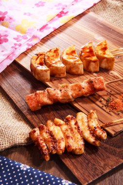 Üç Japon stili şiş, iki tavuk eti ve baharatlı soya peyniri ya da soya peyniri ve çuval bezi kumaşlı bir tahta üzerinde servis edilen yüksek kaliteli bir stok fotoğrafı.