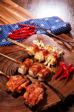 Üç farklı ızgara domuz pastırmasının kaliteli bir fotoğrafı. Söndürülmüş domuz pastırması, dürülmüş mochi, istiridye ve kırmızı biberli tavuk budu. Çuval bezi kumaşlı bir tahta üzerinde.