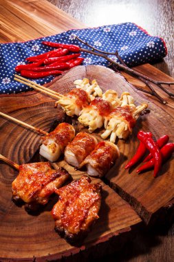 Üç farklı ızgara domuz pastırmasının kaliteli bir fotoğrafı. Söndürülmüş domuz pastırması, dürülmüş mochi, istiridye ve kırmızı biberli tavuk budu. Çuval bezi kumaşlı bir tahta üzerinde.