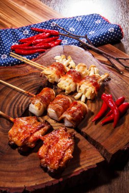 Üç farklı ızgara domuz pastırmasının kaliteli bir fotoğrafı. Söndürülmüş domuz pastırması, dürülmüş mochi, istiridye ve kırmızı biberli tavuk budu. Çuval bezi kumaşlı bir tahta üzerinde.