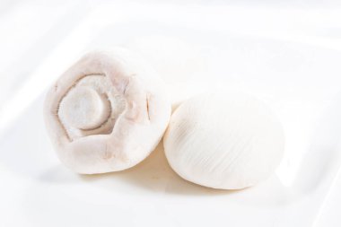 Agaricus bisporus 'un beyaz bir tabakta bulunan iki taze beyaz mantarın yüksek kalite stok fotoğrafı taze dokularını ve doğal renklerini sığ bir alan derinliğiyle vurguluyor.