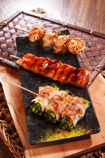 Üç şişe deniz tarağı, jöleli tavuk ve ete sarılmış kuşkonmaz benekli siyah bir tabakta servis ediliyor..