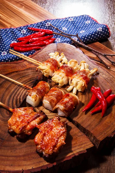 Üç farklı ızgara domuz pastırmasının kaliteli bir fotoğrafı. Söndürülmüş domuz pastırması, dürülmüş mochi, istiridye ve kırmızı biberli tavuk budu. Çuval bezi kumaşlı bir tahta üzerinde.