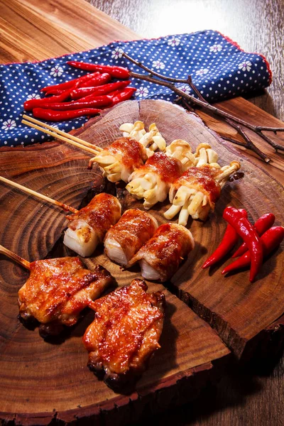 Üç farklı ızgara domuz pastırmasının kaliteli bir fotoğrafı. Söndürülmüş domuz pastırması, dürülmüş mochi, istiridye ve kırmızı biberli tavuk budu. Çuval bezi kumaşlı bir tahta üzerinde.