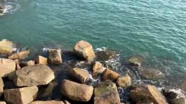 Şafak vakti sakin sahilde engebeli taşlara çarpan güzel dalgalar huzurlu bir sahil atmosferi yaratıyor.