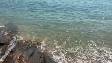 Dalgalar güneşli bir öğleden sonra sakin bir sahil noktasında kayalık sahili nazikçe öperler.