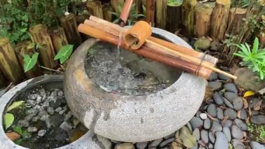 Huzurlu bir bahçede, bambu aksanlı ve doğal bir ortamda, huzurlu bir su damlıyor.