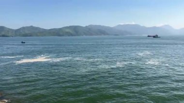 Yumuşak dalgalar, parlak gökyüzünün altındaki sakin dağların arasında tekneleri kucaklıyor.