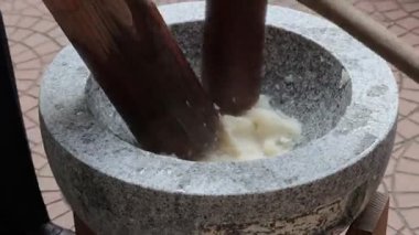 Öğleden sonra güneşinde kültürel bir toplantıda geleneksel bir taş havan topunda pirinç dövmek.