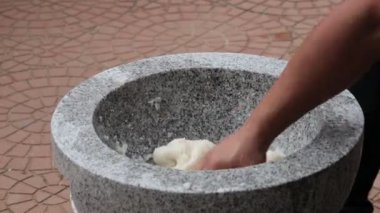 Güneşli bir alanda havan taşı kullanarak geleneksel hamuru yaratmak, sanatsal beceriler ve kültürel miras sergilemek.