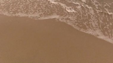 Yumuşak dalgalar gün batımında kumlu sahili nazikçe okşar, sahil boyunca altın renklerde sakin bir manzara çizer.