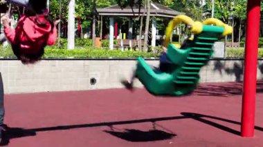 Neşeli bir öğleden sonra oyun saatinde parlak güneşin altında neşeli bir parkta sallanan çocuklar.