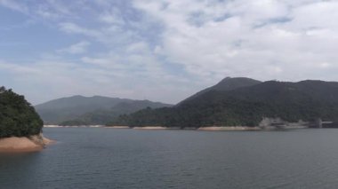 Sakin göl kıyısında uzak dağlar ve nazik dalgalarla aydınlık mavi gökyüzünün altında