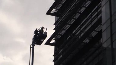 Vişne toplayıcısı işçiler bulutlu bir gökyüzünün altındaki bina bakımı için çok yükseklere ulaşıyor.