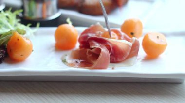 Güneş ışığında taze yeşillik ve canlı kavunun etrafına sarılmış lezzetli jambonun tadını çıkarıyorum.